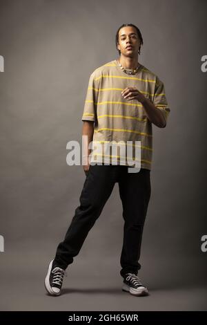 Young African American male model with braided hair dressed in oversized striped shirt and necklace looking at camera against gray background Stock Photo