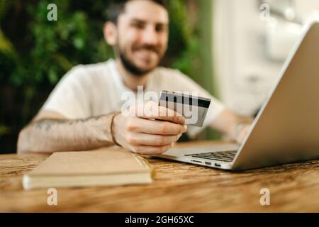 Crop male making purchase with plastic card for order during online shopping via laptop Stock Photo