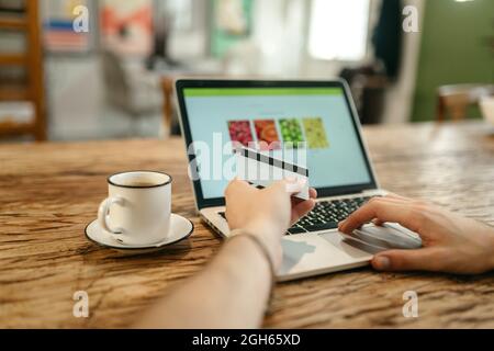 Crop unrecognizable male making purchase with plastic card for order during online shopping via laptop Stock Photo