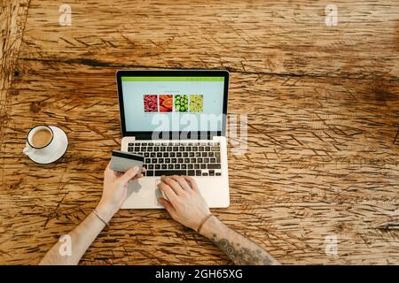 Crop unrecognizable male making purchase with plastic card for order during online shopping via laptop Stock Photo