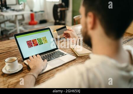 Crop unrecognizable male making purchase with plastic card for order during online shopping via laptop Stock Photo