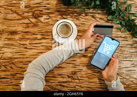 From above of crop unrecognizable female with plastic card making purchase for order and using mobile application for online shopping on smartphone wh Stock Photo