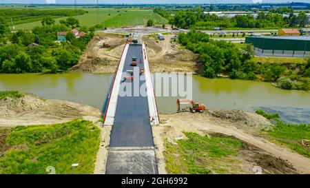Above view, on workers and machinery for laying asphalt, spreading layer of hot tarmac over new bridge, road over river is under construction, buildin Stock Photo