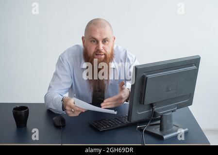 Portrait of a bald man at a desk looking at a report and cursing. The dissatisfied boss dismisses the subordinate. Stock Photo