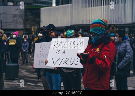 VANCOUVER, CANADA - Apr 12, 2021: A man holding up the "Racism is a virus" sign at a stop Asian hate protest in Vancouver, Canada Stock Photo