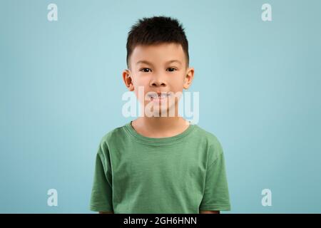 Portrait of little asian boy in green t-shirt posing over blue background Stock Photo