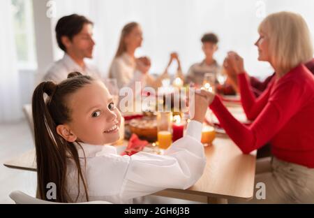 Happy little girl with family saying prayer before festive Thanksgiving or Christmas dinner, celebrating holiday at home Stock Photo