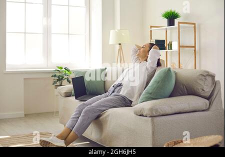 Woman sitting on sofa with hands behind head, relaxing, feeling happy and satisfied Stock Photo