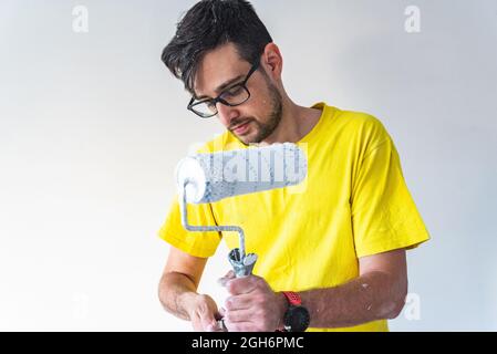 Concentrated man using a paintbrush roller on a stick to paint the ceiling. Stock Photo
