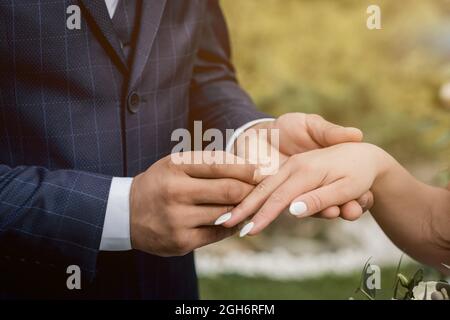 couple exchanging wedding rings during their wedding ceremony outdoors. Cropped shot of groom putting a wedding ring on the finger of the bride. Stock Photo