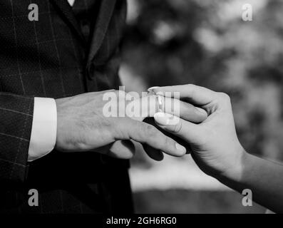 Couple exchanging wedding rings during their wedding ceremony. Cropped shot of groom putting a wedding ring. Black and white image Stock Photo