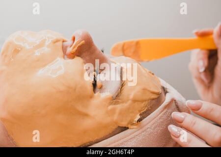 Using a gold mask in cosmetology, a woman at a beautician applying a gold mask on her face. new Stock Photo