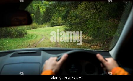 Driver driving a modern off road right hand drive RHD car on the mountain green forest country road. Face reflecting in inside mirror. POV inside car Stock Photo