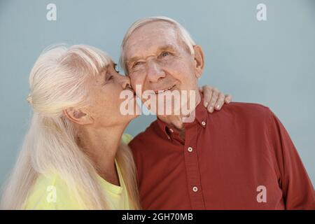 Blonde mature woman kisses loving partner standing on light grey background Stock Photo