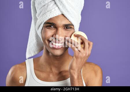 Portrait of handsome man cleaning face and looking camera with cosmetic pads on purple background Stock Photo
