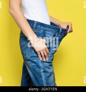 The concept of diet, proper nutrition, weight loss. Slim Woman Showing Loose Jeans and her Loss Weight. Woman white t-shirt and oversize jeans Stock Photo