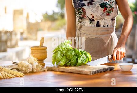 hands of Woman chopping green basil at kitchen table in a garden outdoor Stock Photo