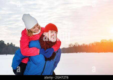 Smiling senior man giving mature woman piggyback in snowy winter park Stock Photo