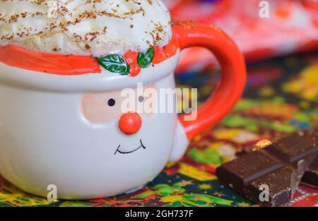 Christmas hot chocolate in Santa face mug with whipped cream and shaved chocolate with chocolate squares on the side. Christmas hot drink. Christmas p Stock Photo