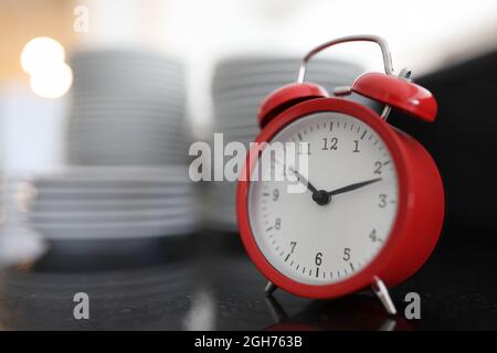 Red alarm clock on background of large stack of plates Stock Photo