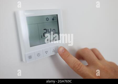 Person regulates air temperature in room through remote control on wall Stock Photo