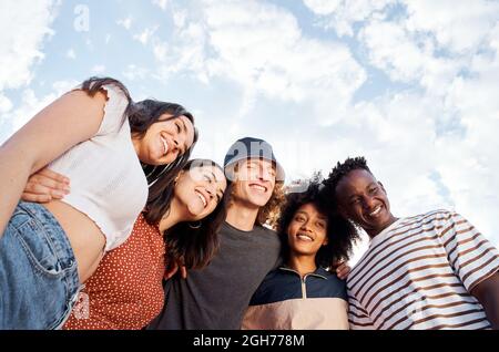 Portrait with copy space from a low angle of a group of smiling young multiethnic people. In the background a beautiful sky with clouds. Stock Photo