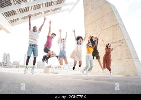 Group of happy multiethnic friends having fun. Young students jumping outside the university. Stock Photo