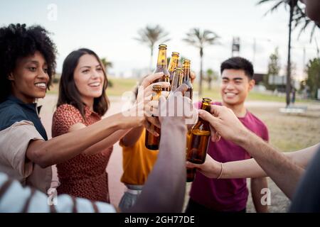 Close-up of hands of a group of young people of different races toasting happily at sunset. Cheers. Stock Photo