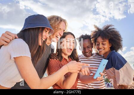 Group of young mixed race people looking at a cell phone while pointing at something funny on the screen. Concept of technology, connection, app Stock Photo