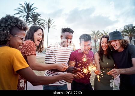 Group of friends smiling and having a good time around some sparklers. Mixed race youngsters enjoy spending time together in summer. Concept of Stock Photo