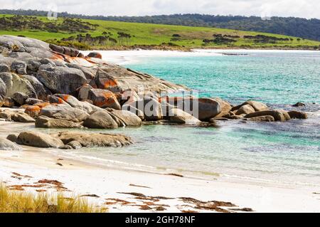 Orange lichen-covered granite boulders in a small white sandy beach - The Gardens, Tasmania, Australia Stock Photo