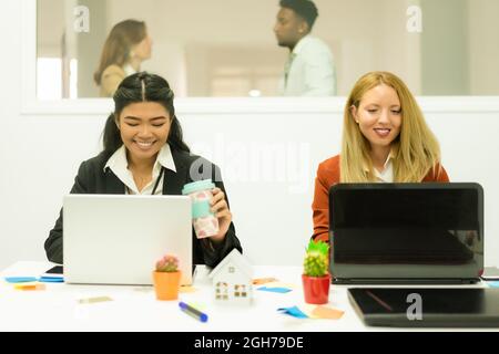 Photo of cheerfuls joyful multiracial women in white shirt and black jacket, smiling and writing with a laptops. Work and study concept. Stock Photo