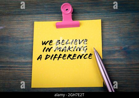 We Believe in Making a Difference. Yellow sticky note on the table. Stock Photo