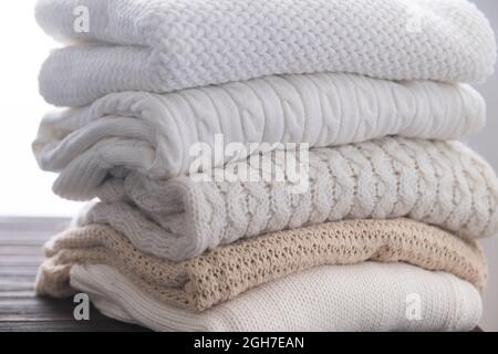 Stack of white cozy knitted sweaters on wooden table Stock Photo