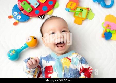 joyful baby lying on his back among toys Stock Photo