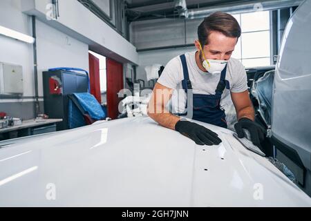 Optimistic car mechanic in process of manual car part sanding Stock Photo