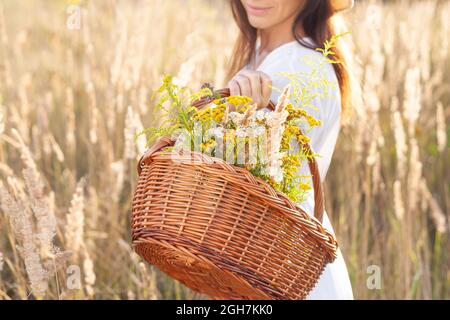 A woman holds a wooden basket with herbs in her hand. Stock Photo