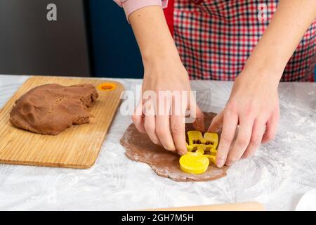 Woman's hands cut out cookies from the dough in the form of ginger man. Close-up of hands. The concept of home cooking and Christmas. Stock Photo
