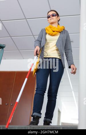blind woman walking down the stairs alone using cane Stock Photo