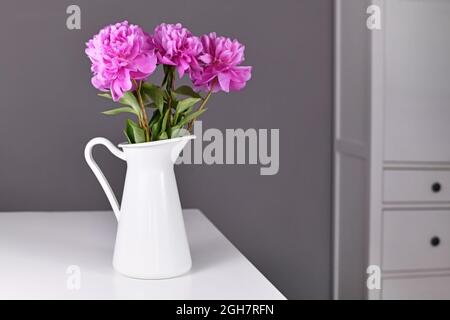 Pink bouquet of Chinese peony flowers in white vase on table in front of gray background Stock Photo