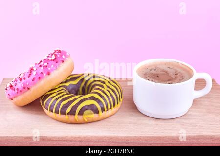 Three bright donuts near with a cup of coffee on a wooden board. Stock Photo