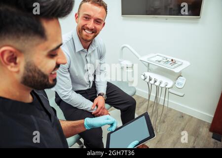 Caucasian male nurse reading off digital tablet explaining process to client sitting in dentist chair Stock Photo