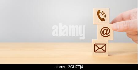 Hand Stacking wood Blocks with Icons mobile phone, email envelope telephone and e-mail address Against gray Background. Wooden cubes with symbol telep Stock Photo