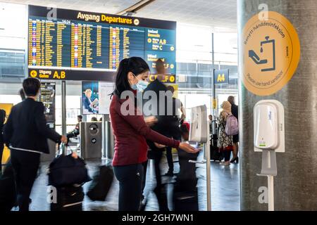 Young woman wearing face mask uses hand sanitizer gel to protect from Covid-19 at the Oslo Gardermoen Airport in Oslo, Norway, Europe Stock Photo