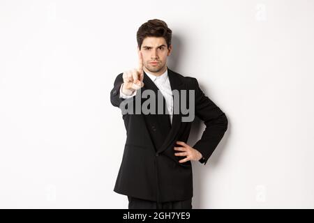 Portrait of serious handsome man in business suit, showing one finger to prohibit or decline something, telling to stop, disagree with you, standing Stock Photo