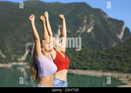 Two women celebrating vacation raising arms in nature on summer