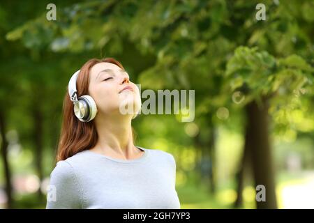 Relaxed woman wearing headphones meditating listening audio guide in a park
