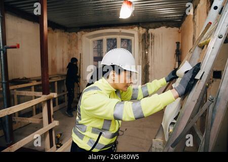 Female building contractor reading blueprint while working at site Stock Photo