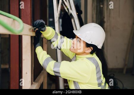 Female engineer marking on wooden plank while working at site Stock Photo