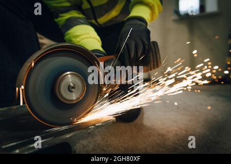 Female worker using electric saw while cutting metal at construction site Stock Photo